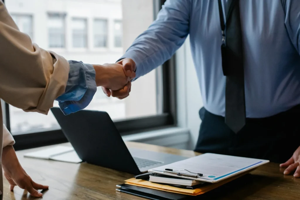 Two people shaking hands over a laptop, symbolizing collaboration and trust in Zechion AI for clinic owners